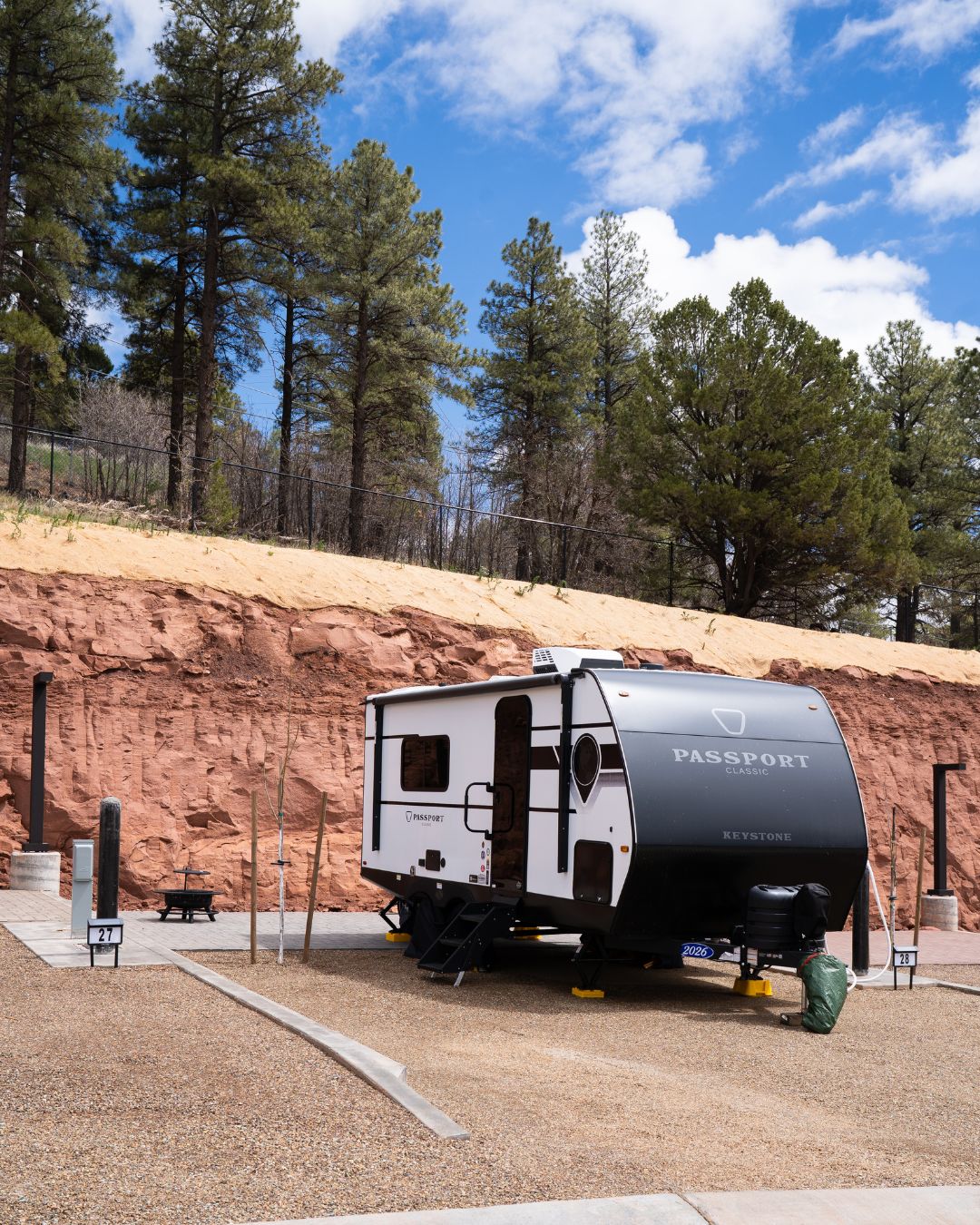 Travel trailer parked at a full-hookup RV site beside red rock and pine trees at Flagstaff Mountain RV.