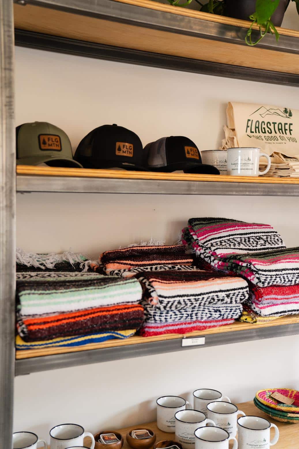 Retail shelves displaying neatly folded, colorful woven blankets, trucker hats with